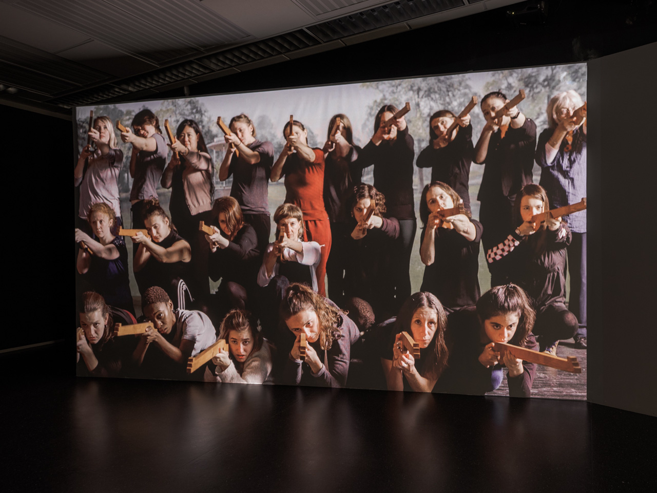 Video artwork of women with wooden guns pointing at the viewer
